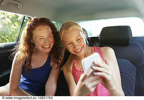 Happy preteen girl friends taking selfie in back seat of car