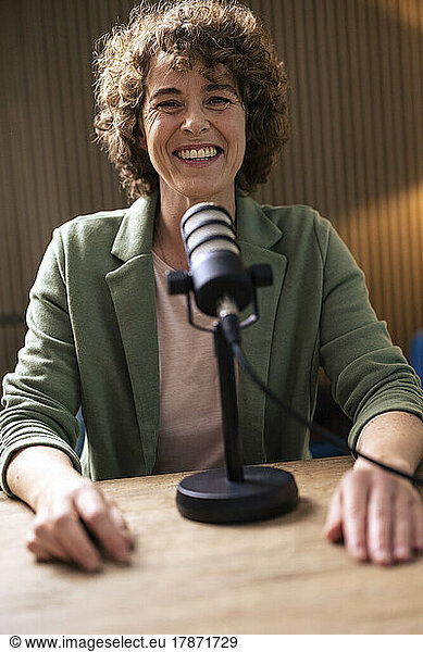 Happy radio DJ with microphone sitting at desk in radio station