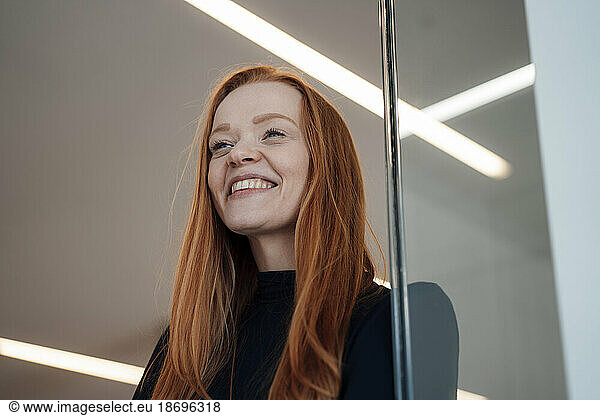 Happy redhead businesswoman near wall at office