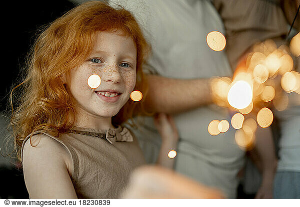Happy redhead girl holding sparkler at home