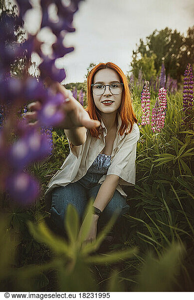 Happy redhead teenage girl crouching amidst lupin flowers