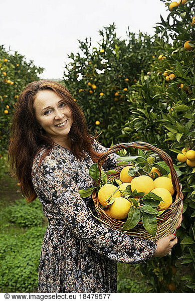 Happy redhead woman standing with basket of oranges