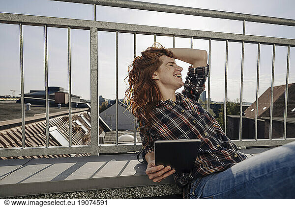 Happy redheaded woman with tablet relaxing on rooftop terrace