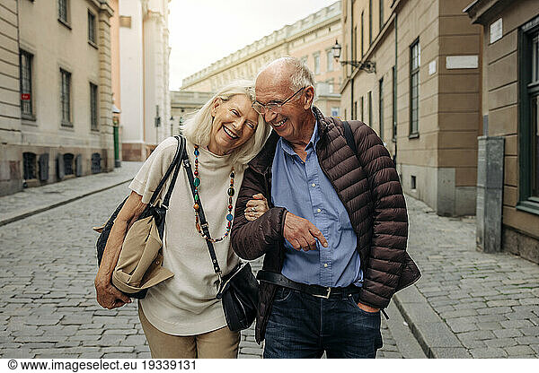 Happy retired senior couple with arm in arm strolling on city street