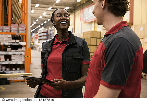 Happy saleswoman holding digital tablet while looking at male sales staff at hardware store