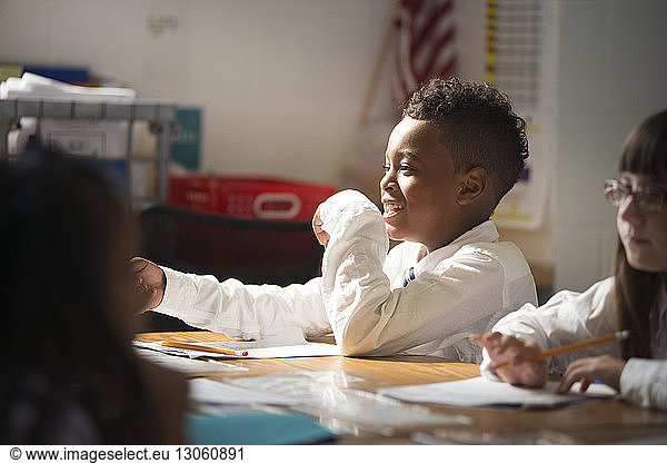 Happy schoolboy sitting with girl at desk in classroom