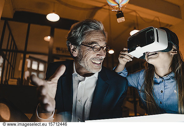 Happy senior buisinessman and girl wearing VR glasses with hot-air balloon in office
