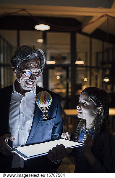 Happy senior buisinessman and girl with hot-air balloon and shining tablet in office