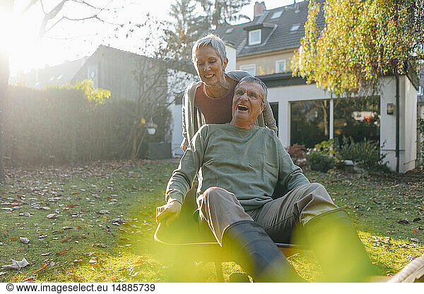 Happy senior couple having fun with wheelbarrow in garden