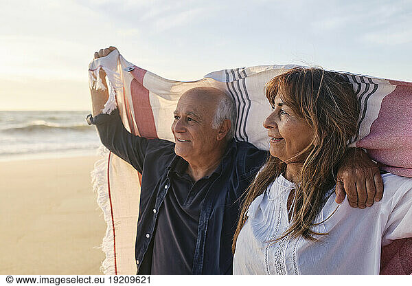 Happy senior couple holding scarf at beach