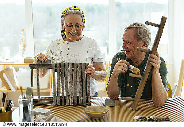 Happy senior couple polishing wood in workshop