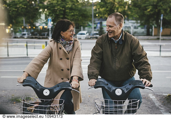Happy senior couple taking rental bikes at parking lot