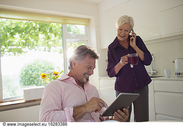 Happy senior couple using digital tablet and smart phone in kitchen