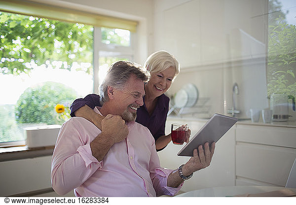 Happy senior couple using digital tablet in kitchen