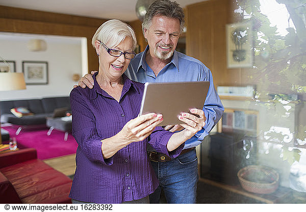 Happy senior couple using digital tablet in living room