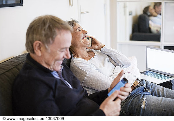 Happy senior couple using smart phones in living room