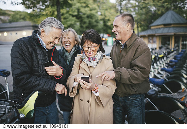 Happy senior couples using mobile phones at bicycle parking station