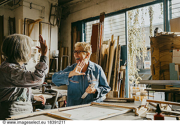 Happy senior craftswomen giving high-five at carpentry workshop