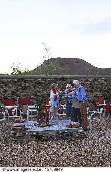Happy senior friends drinking wine at hotel patio fire pit