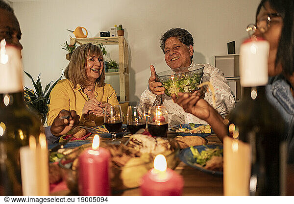 Happy senior friends enjoying dinner with candles on table at home