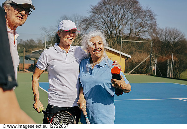 Happy senior friends looking away while holding tennis racket at court