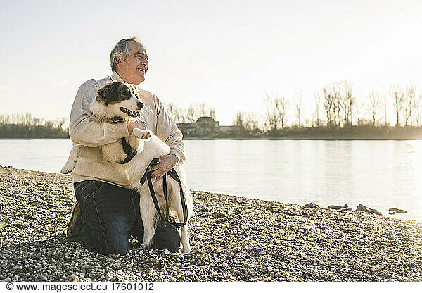 Happy senior man embracing dog at beach on sunny day
