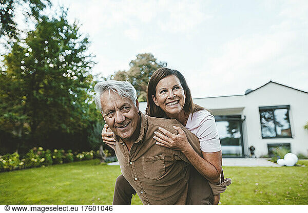 Happy senior man giving piggyback ride to cheerful woman at backyard