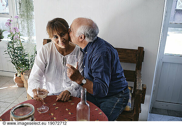 Happy senior man kissing woman with glasses of wine in cafe