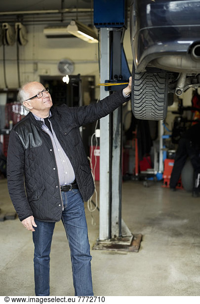 Happy senior man looking at car lifted on jack at auto repair shop