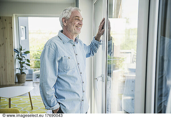 Happy senior man looking through window at home