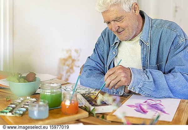 Happy senior man painting with watercolor paints on table at home