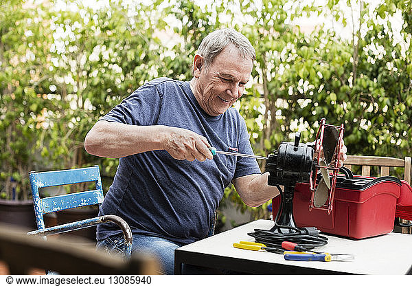 Happy senior man repairing electric fan at yard