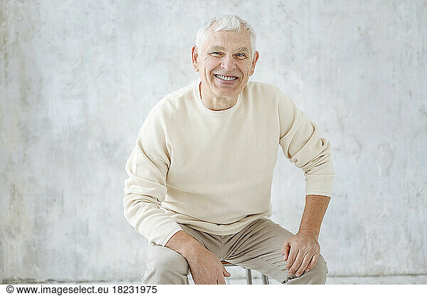 Happy senior man sitting on stool in front of wall at home