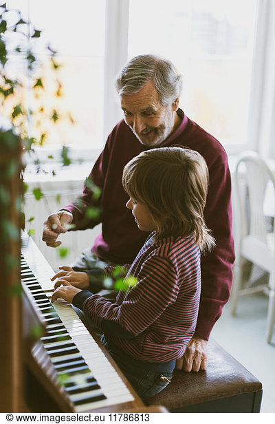 Happy senior man talking to great grandfather playing piano at home