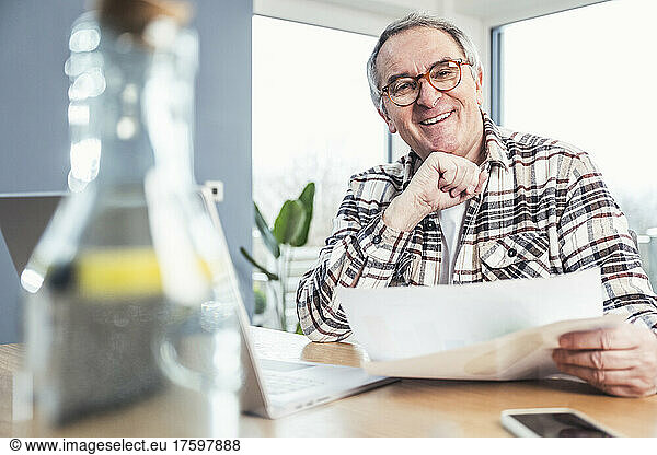 Happy senior man wearing eyeglasses sitting with financial bill at table