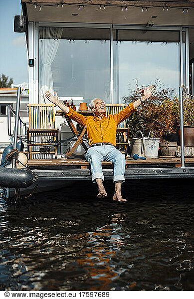Happy senior man with arms outstretched sitting at houseboat enjoying on sunny day