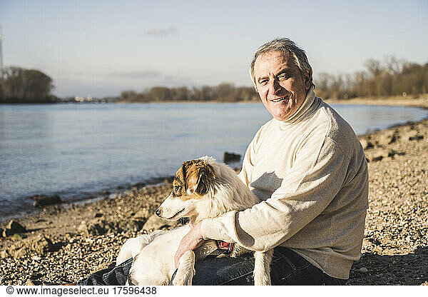 Happy senior man with dog sitting at beach on sunny day