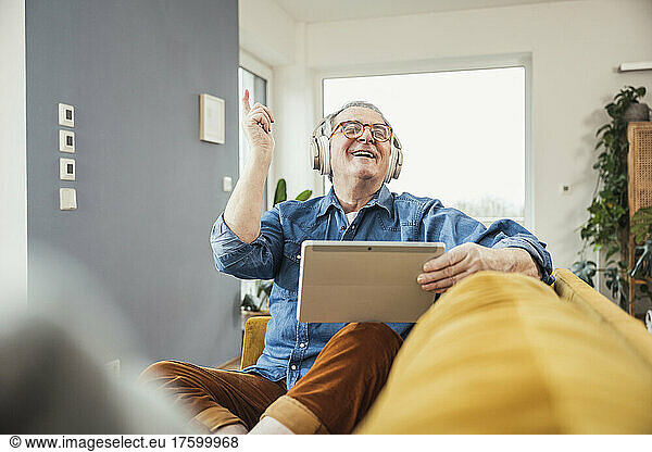 Happy senior man with eyes closed enjoying music through wireless headphones in living room