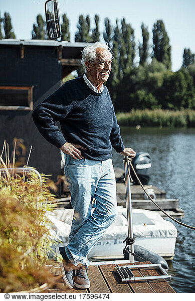 Happy senior man with hand on hip standing at houseboat