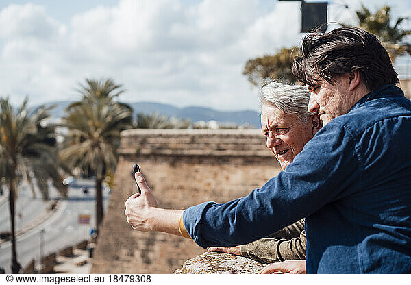 Happy senior man with son taking selfie through smart phone on sunny day