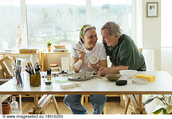Happy senior man with woman painting ceramic cup in workshop