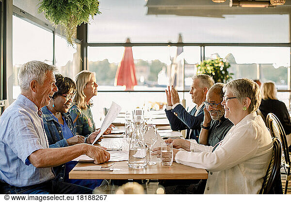 Happy senior men and women talking with each other while sitting together at table in restaurant