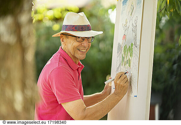 Happy senior wearing hat drawing in garden