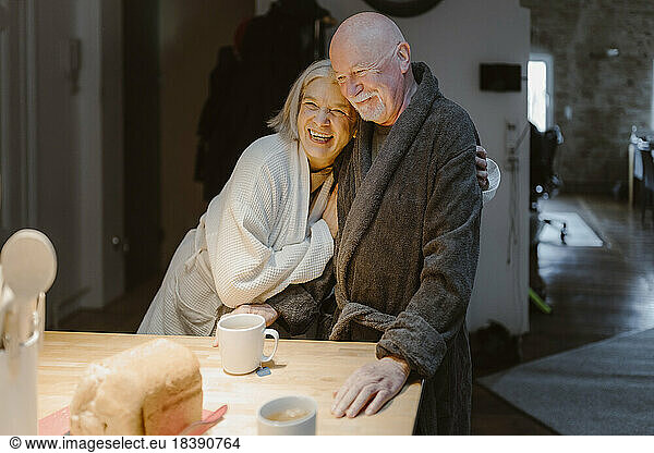 Happy senior woman embracing man wearing bathrobe at home
