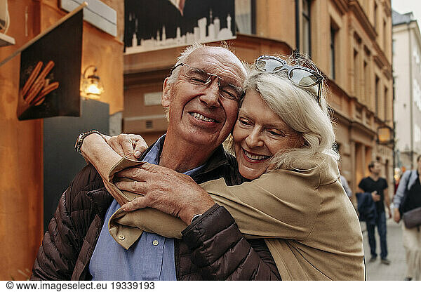 Happy senior woman hugging man from behind in city