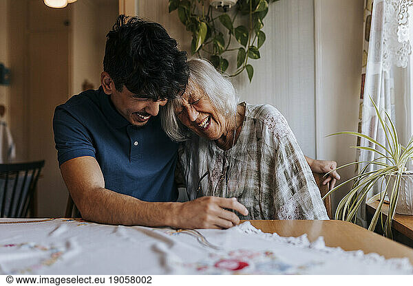 Happy senior woman leaning on male caregiver's shoulder at home