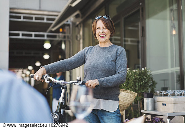 Happy senior woman looking away while holding bicycle outdoors