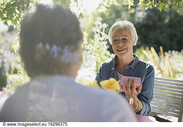 Happy senior woman opening gift from husband on sunny summer patio