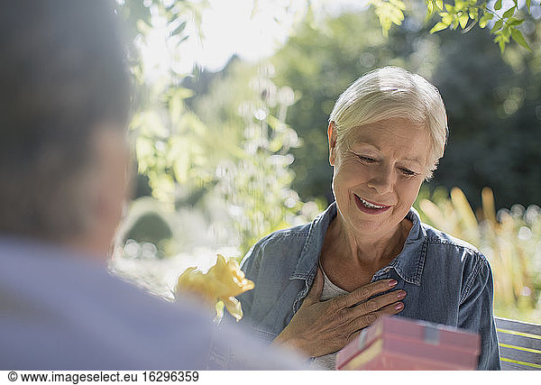 Happy senior woman receiving gift from husband on sunny patio
