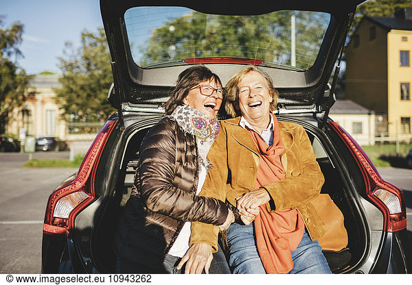 Happy senior woman sitting in opened car trunk